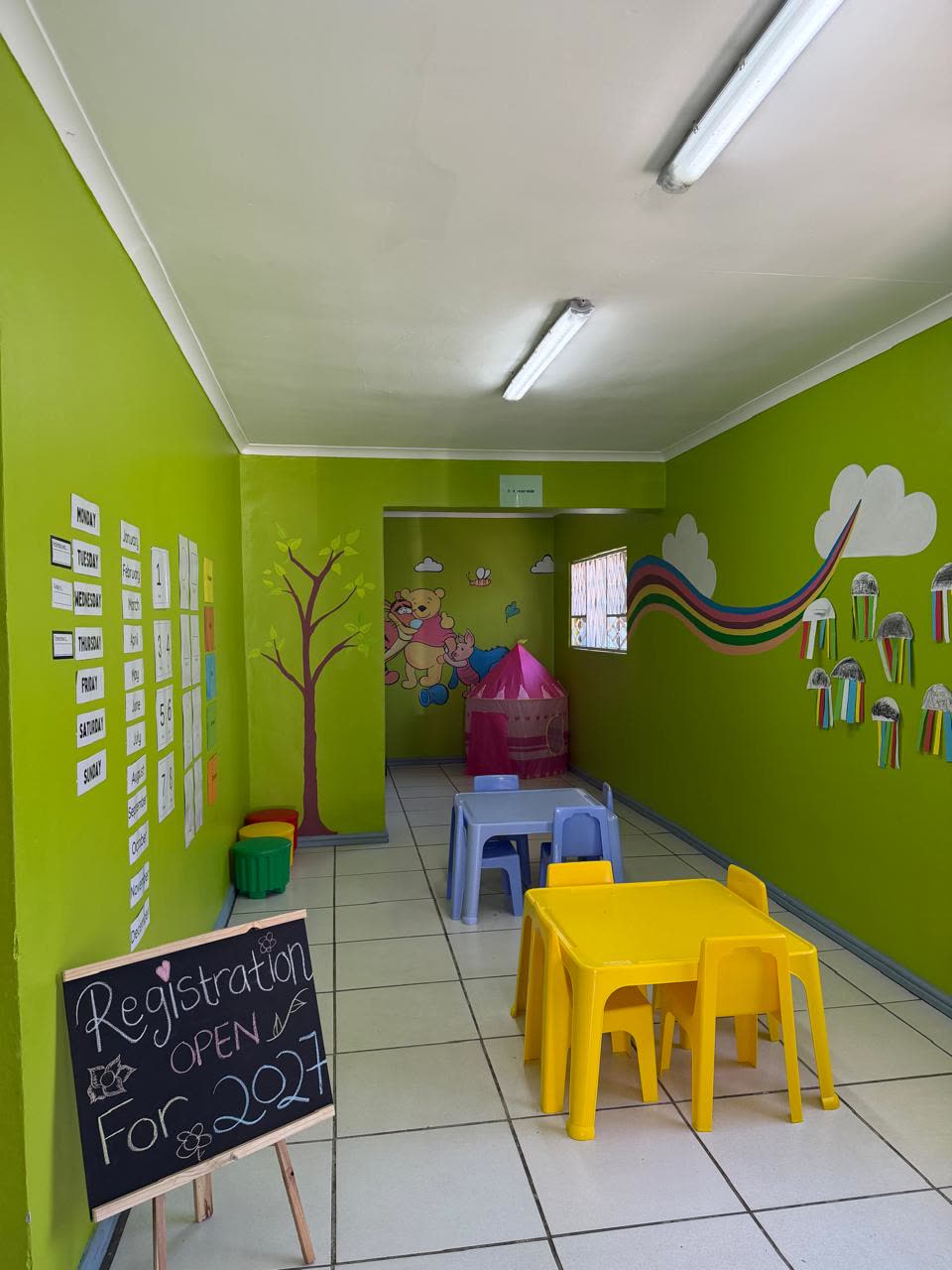 A preschool classroom with child-height tables, a days-of-the-week wall chart and children’s artwork on display