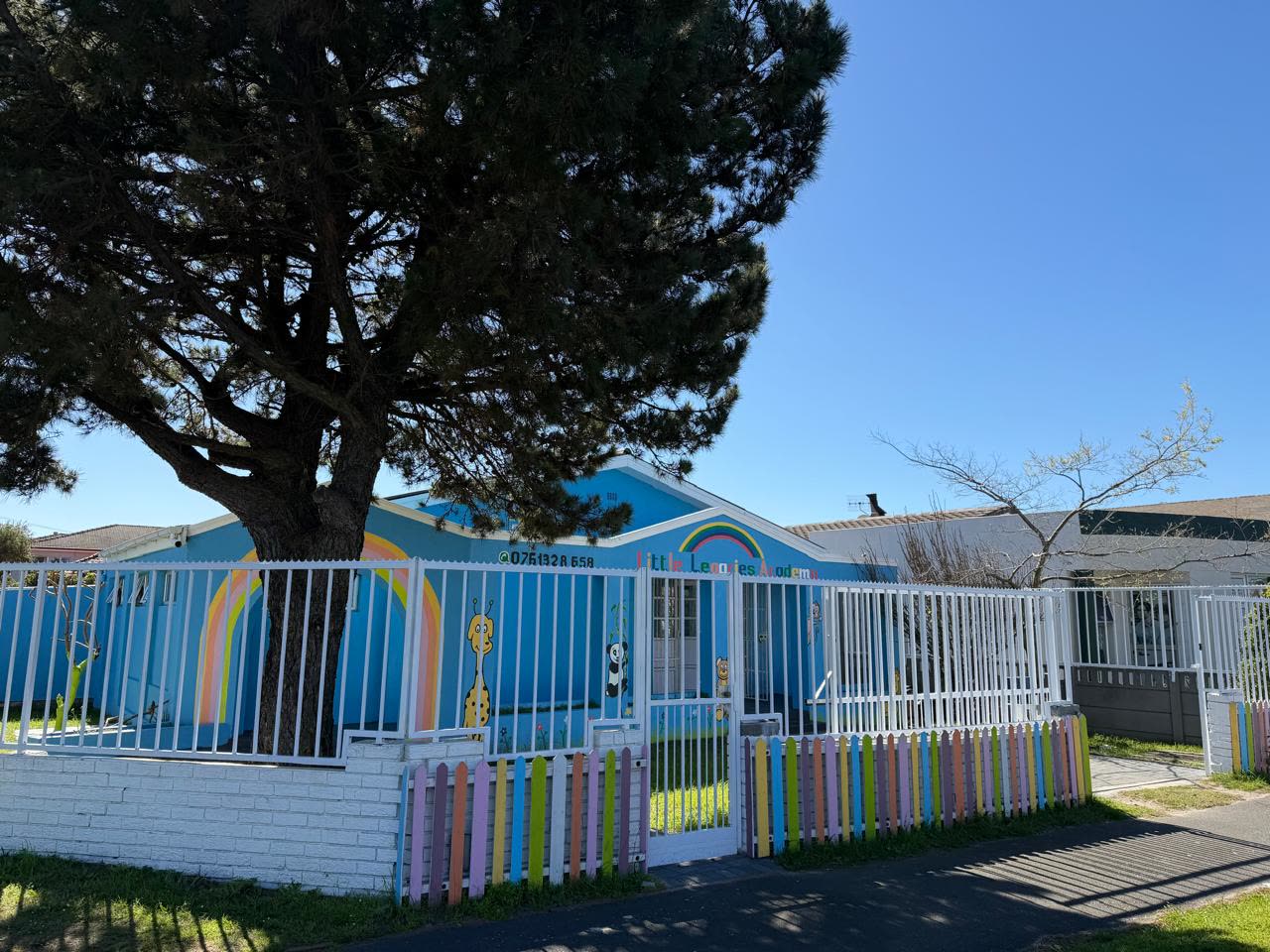 Little Legacies Academy seen from 67 Kromboom Road, enclosed by a white palisade fence and a colourful picket fence